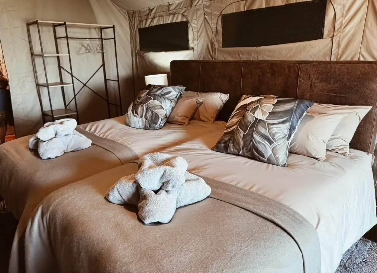 Neatly dressed bed with folded towels inside a Nyime luxury tent